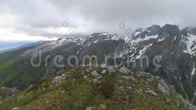 一个徒步旅行者<strong>站在山顶</strong>上，看着白雪皑皑的山脉，举起双手做胜利的手势。